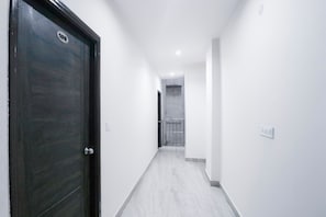 A hallway with a dark wooden door on the left, white walls, and a tiled floor. - Hotel O Kings Inn (Ludhiana)