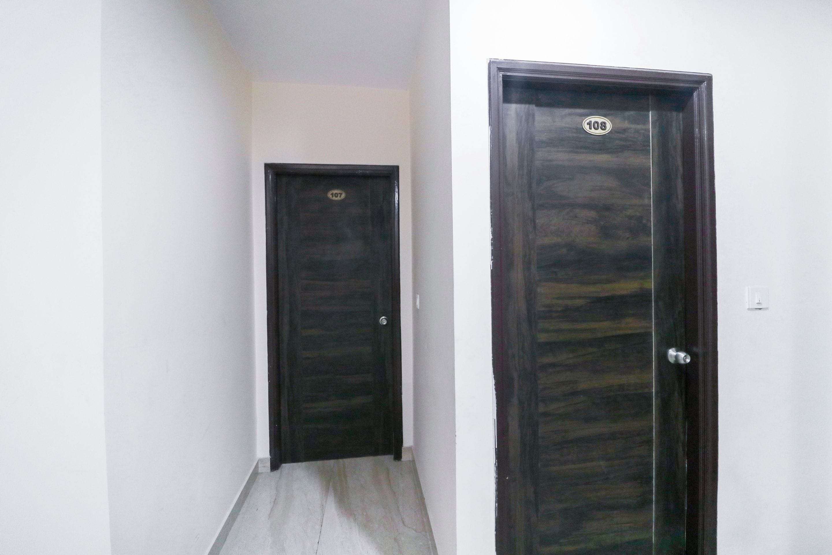 Un pasillo estrecho con dos puertas de madera oscura, una con una placa de identificación visible.