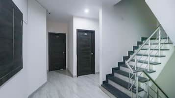 A hallway with two dark doors, a staircase with metal railings, and a light-colored tiled floor.