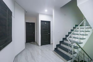 A hallway with two dark doors, a staircase with metal railings, and a light-colored tiled floor. - Hotel O Kings Inn (Ludhiana)