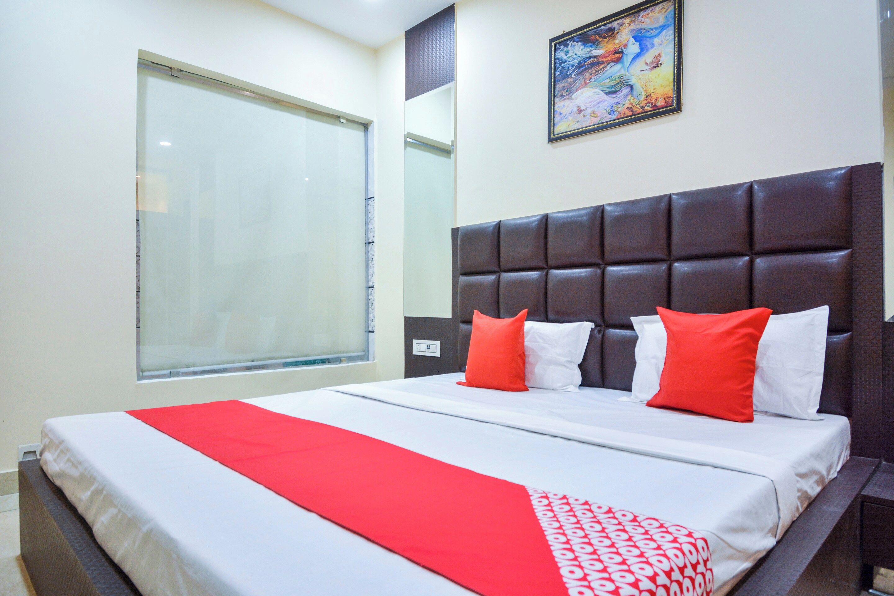 A hotel room with a large bed, a window, and a painting on the wall.