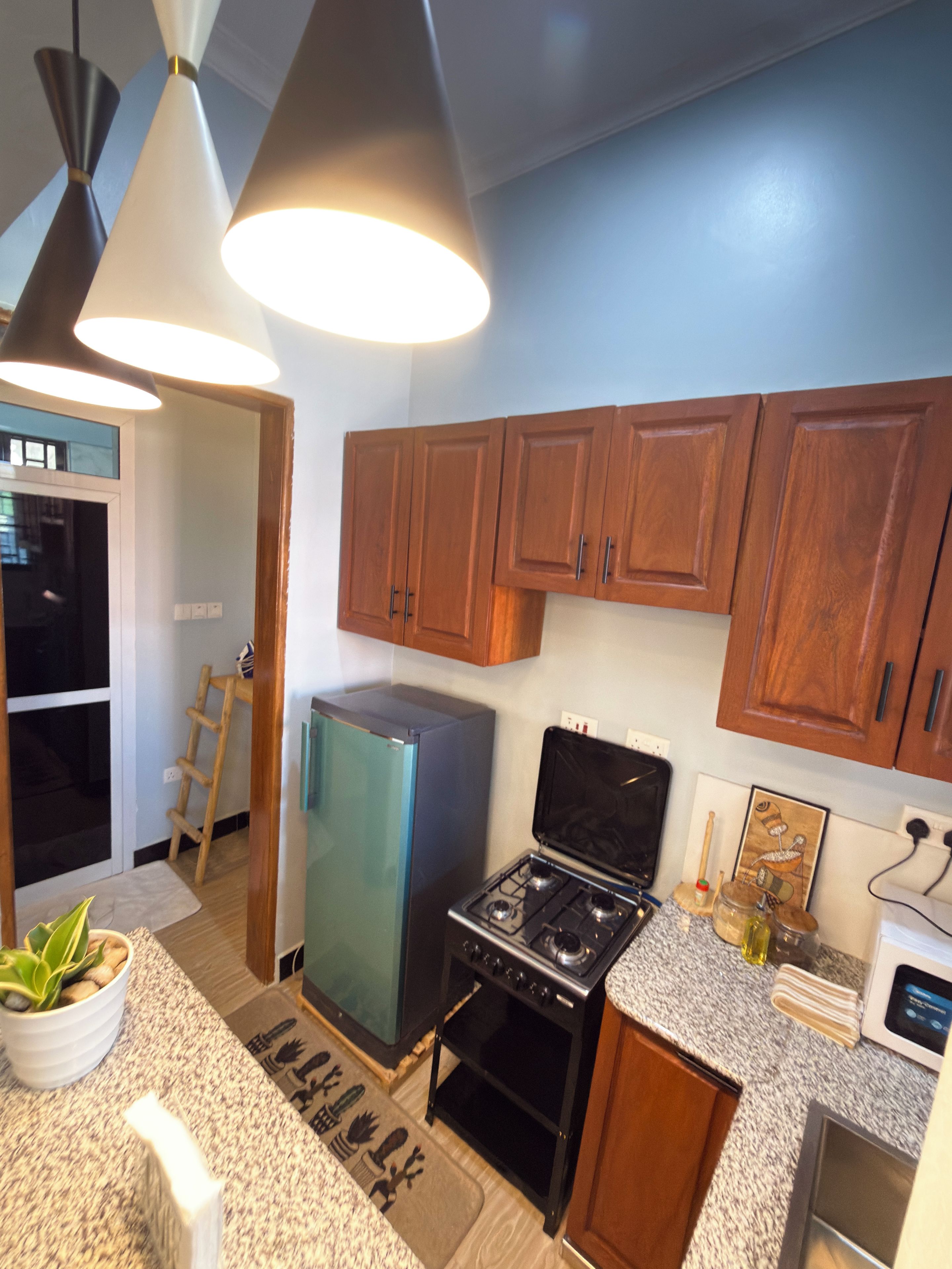 Une cuisine avec des meubles de rangement en bois, un réfrigérateur, une cuisinière et des luminaires suspendus.
