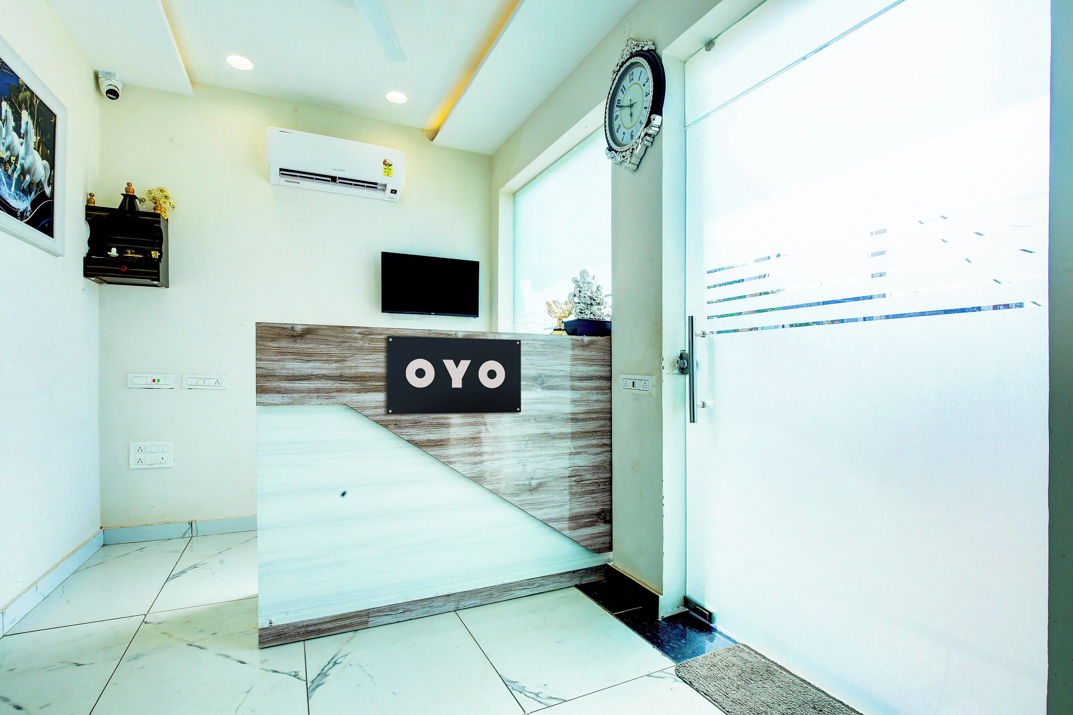 A reception area with a reception desk labeled 'OYO,' a mounted television, and an air conditioning unit on the wall.