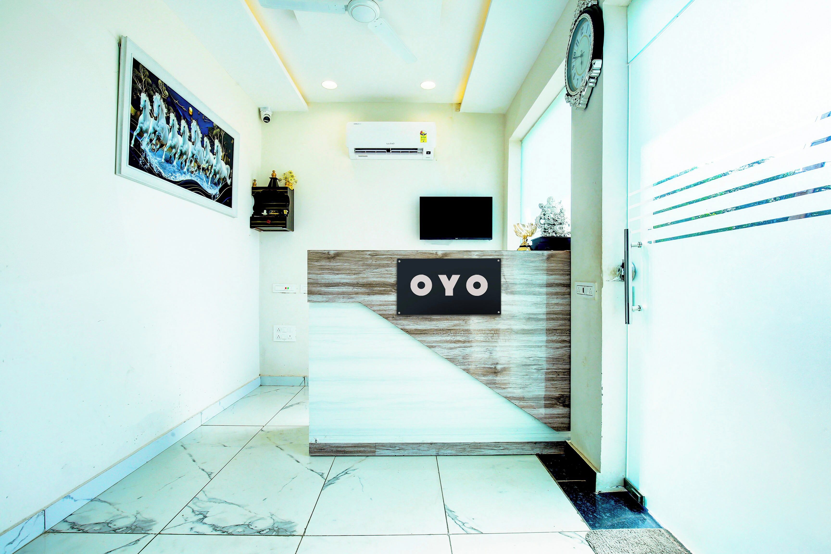 Un área de recepción con mostrador identificada con 'OYO', un reloj de pared, un televisor de pantalla plana y un equipo de aire acondicionado instalado en la pared.