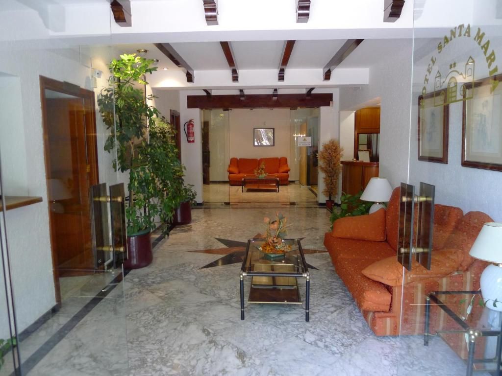 Um hall de hotel com design moderno, destacando uma mesa de centro de vidro, um sofá e plantas em vasos.