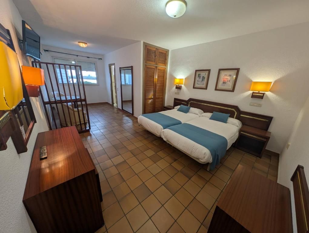 Quarto de hotel com cama, escrivaninha e cadeira. Há uma janela e uma porta.