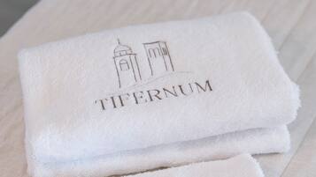 Deux serviettes blanches pliées, portant l’inscription « TIFERNUM » et une illustration représentant un bâtiment, sont posées sur une surface en bois.