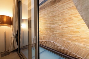 Habitació amb porta de vidre que dona a una paret de pedra, una làmpada de peu i vista cap a l'exterior.