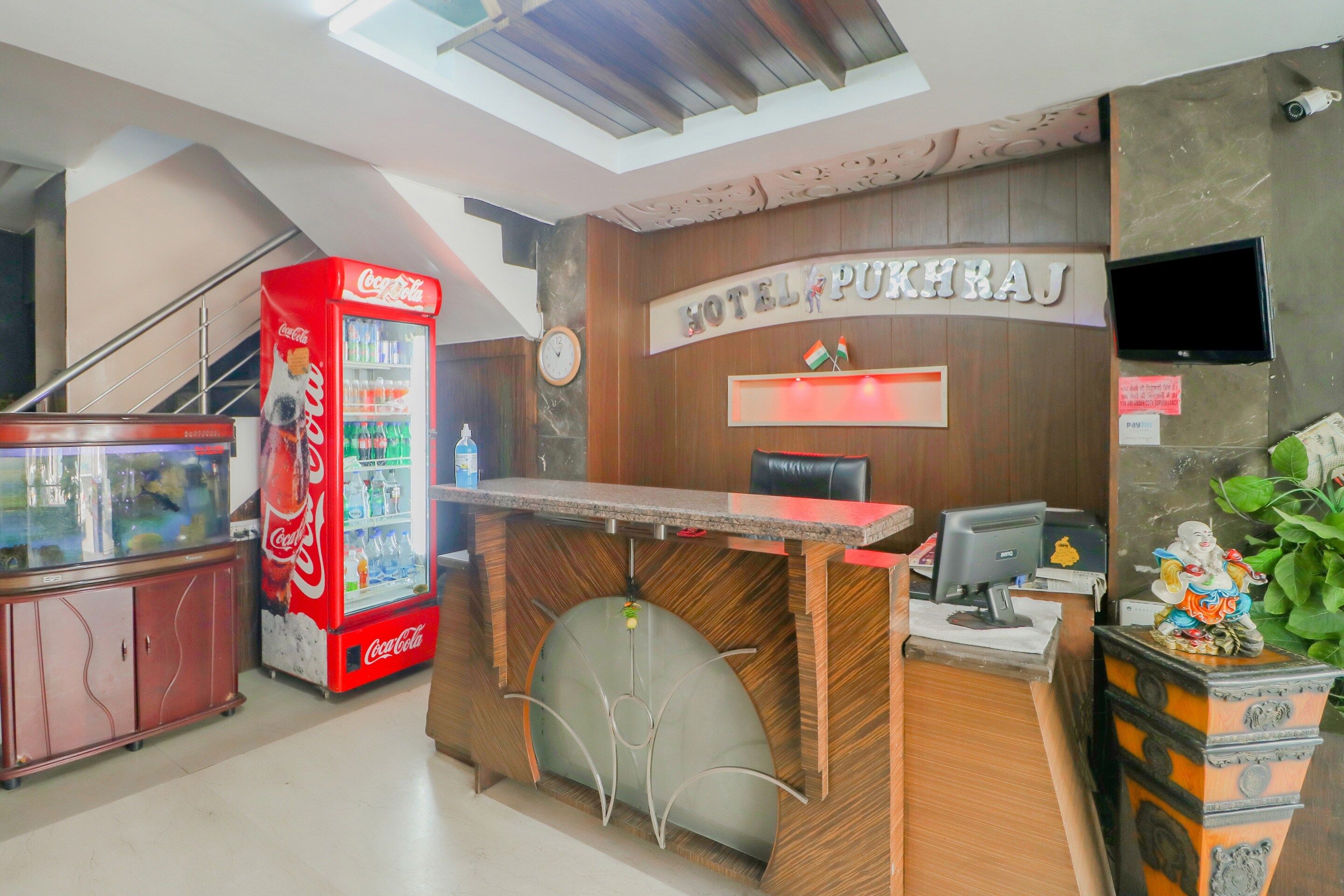 Un mostrador de recepción de hotel con una máquina expendedora de Coca-Cola, un reloj y una pantalla de televisión.