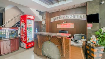 Un mostrador de recepción de hotel con una máquina expendedora de Coca-Cola, un reloj y una pantalla de televisión.