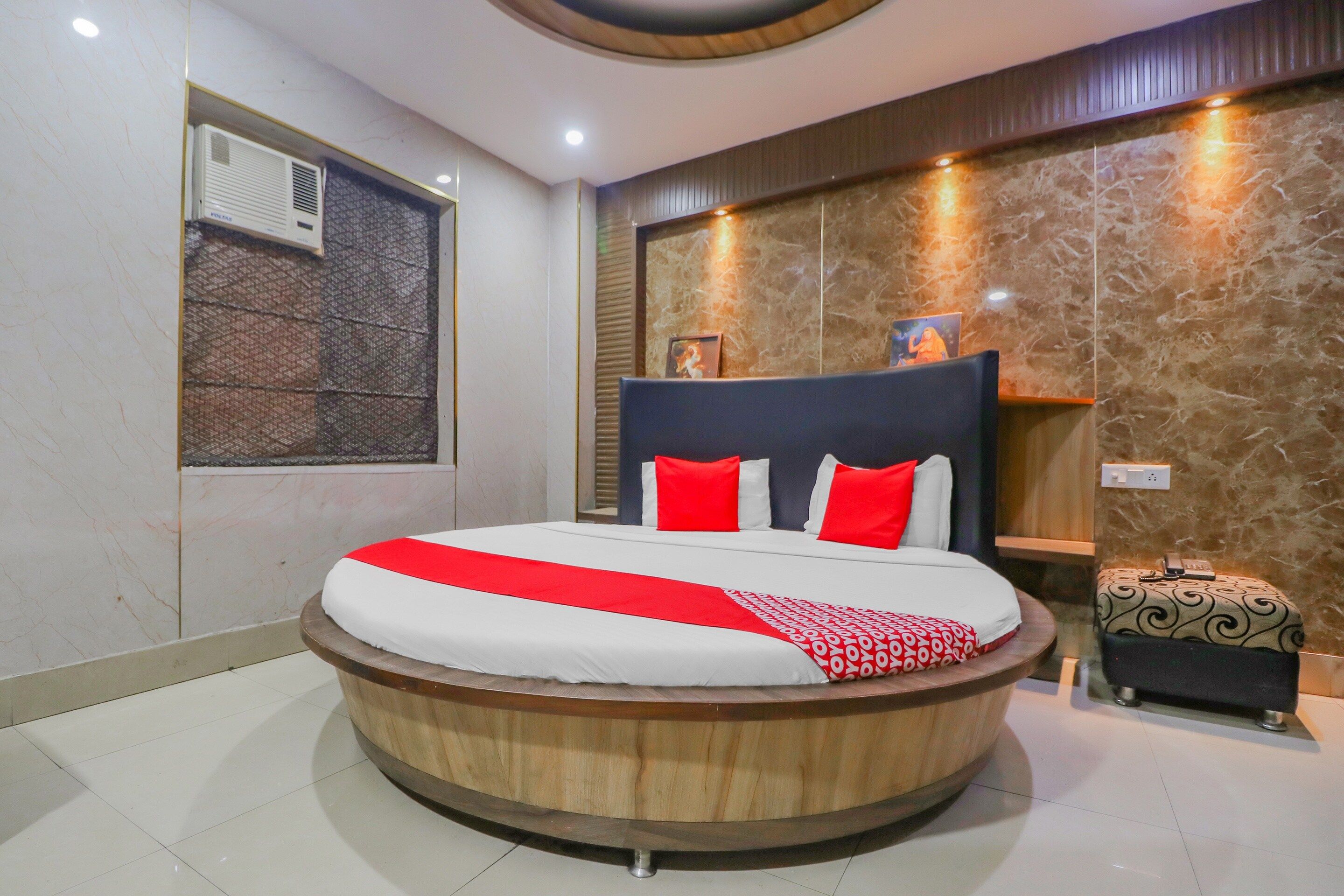 A circular bed with a wooden frame, red and white bedding, and a red throw.