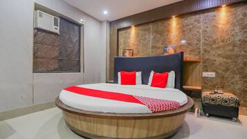 A circular bed with a wooden frame, red and white bedding, and a red throw.