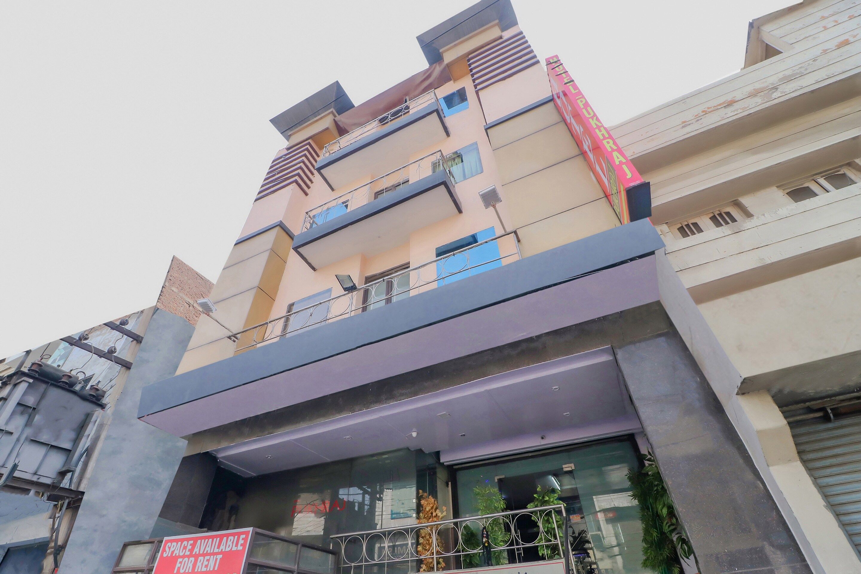 Un edificio de varios pisos con balcones, un cartel que indica espacio disponible para alquiler y un local comercial con puertas de vidrio.
