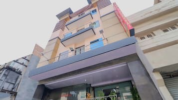 Un edificio de varios pisos con balcones, un cartel que indica espacio disponible para alquiler y un local comercial con puertas de vidrio.
