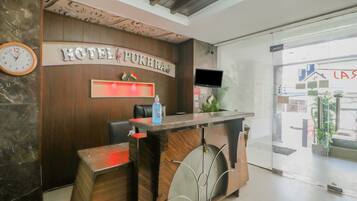 A hotel reception desk with a clock, a sign reading 'HOTEL PUKHRAJ', and a television mounted on the wall.