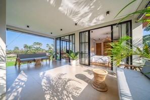 An open-plan living area with a sofa, a bench, and a dining table, featuring large windows and indoor plants. - Elegant 5BR Villa in Tropical Ubud with Pool+Patio (Gianyar Regency)