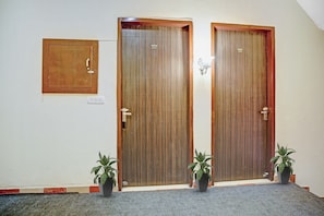 Dos puertas de madera con los números 202 y 201, un espejo pequeño cuadrado y dos plantas en macetas sobre un suelo alfombrado.