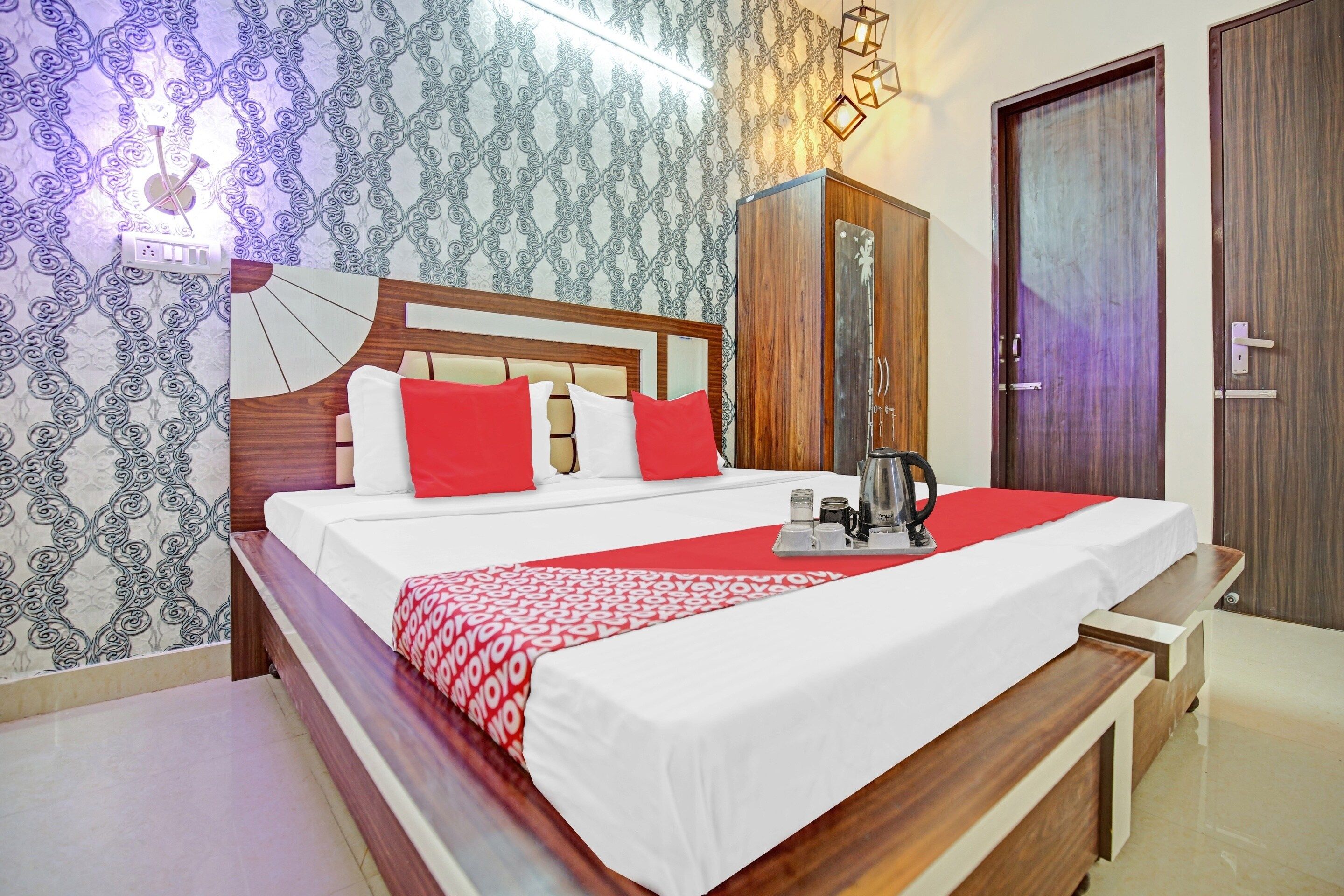 A neatly made bed with red and white bedding, a wooden headboard, and a bedside table with a kettle and cups.