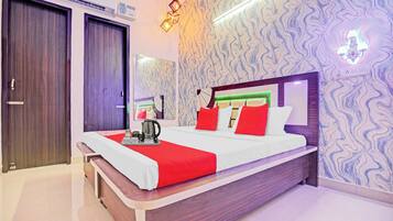 Una habitación de hotel con cama, cafetera y lámpara de pared.