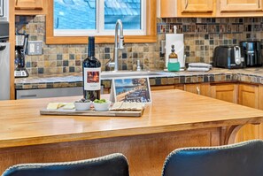 A kitchen with a wooden table set for a meal, a wine bottle, and a welcome card. - Hot Tub + Pine-View Decks • Near Speedboat Beach + Crystal Bay | Emberpine (Kings Beach)