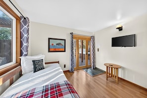 Une chambre à coucher comprenant un lit, un téléviseur, une petite table en bois et une porte donnant sur un espace extérieur.