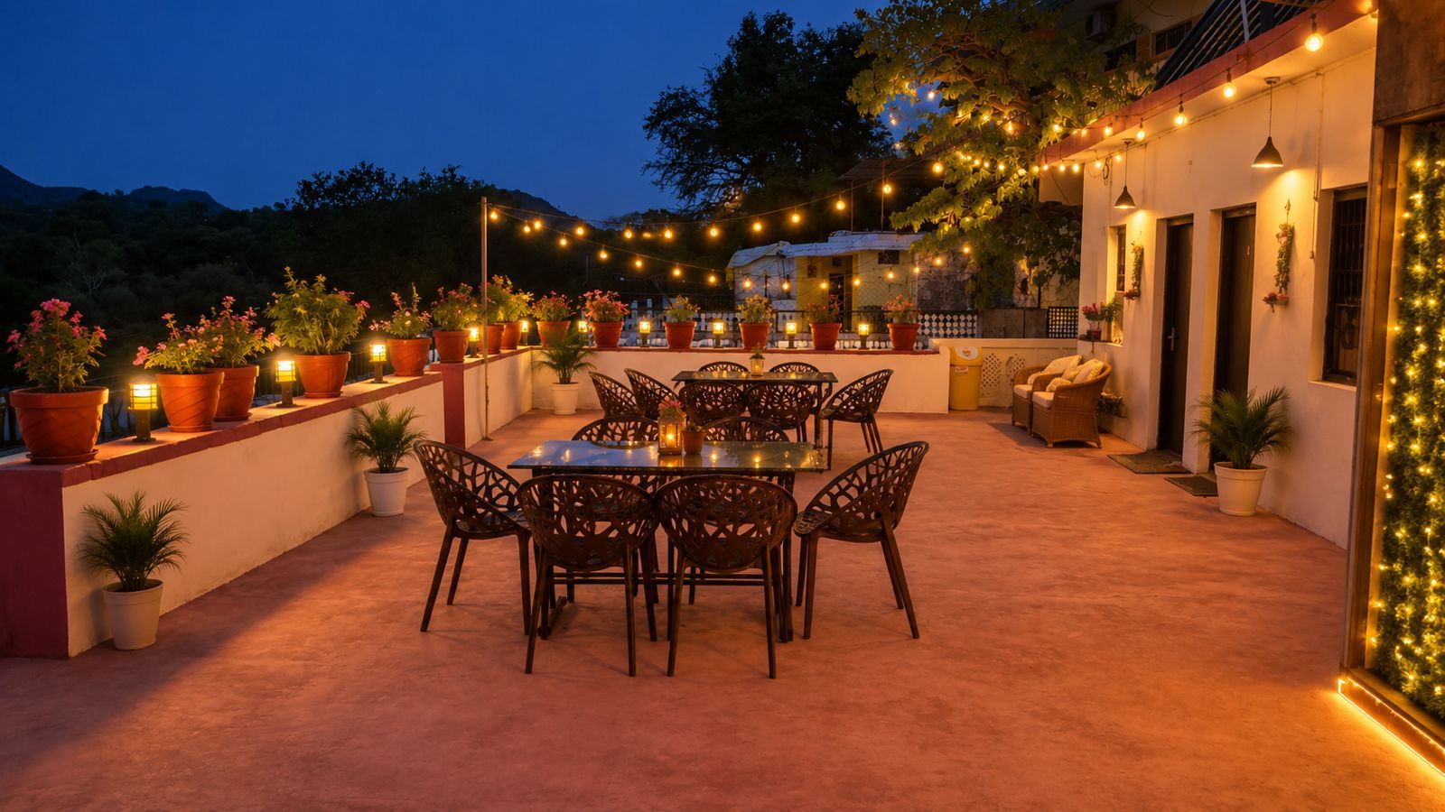 Un espace extérieur aménagé en terrasse, avec une table et des chaises, entouré de plantes en pot et illuminé de guirlandes lumineuses.