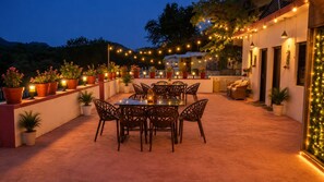 Un espacio al aire libre con patio, una mesa y sillas para comer, rodeado de plantas en macetas y luces colgantes.