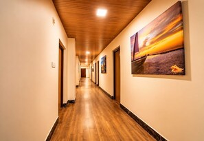A hotel corridor with wooden flooring, a wooden ceiling, and a sunset painting on the wall. - Hotel Lasa inn (Abu)