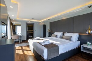 A modern hotel room with a large bed, bedside tables, a desk, and a view of the city.