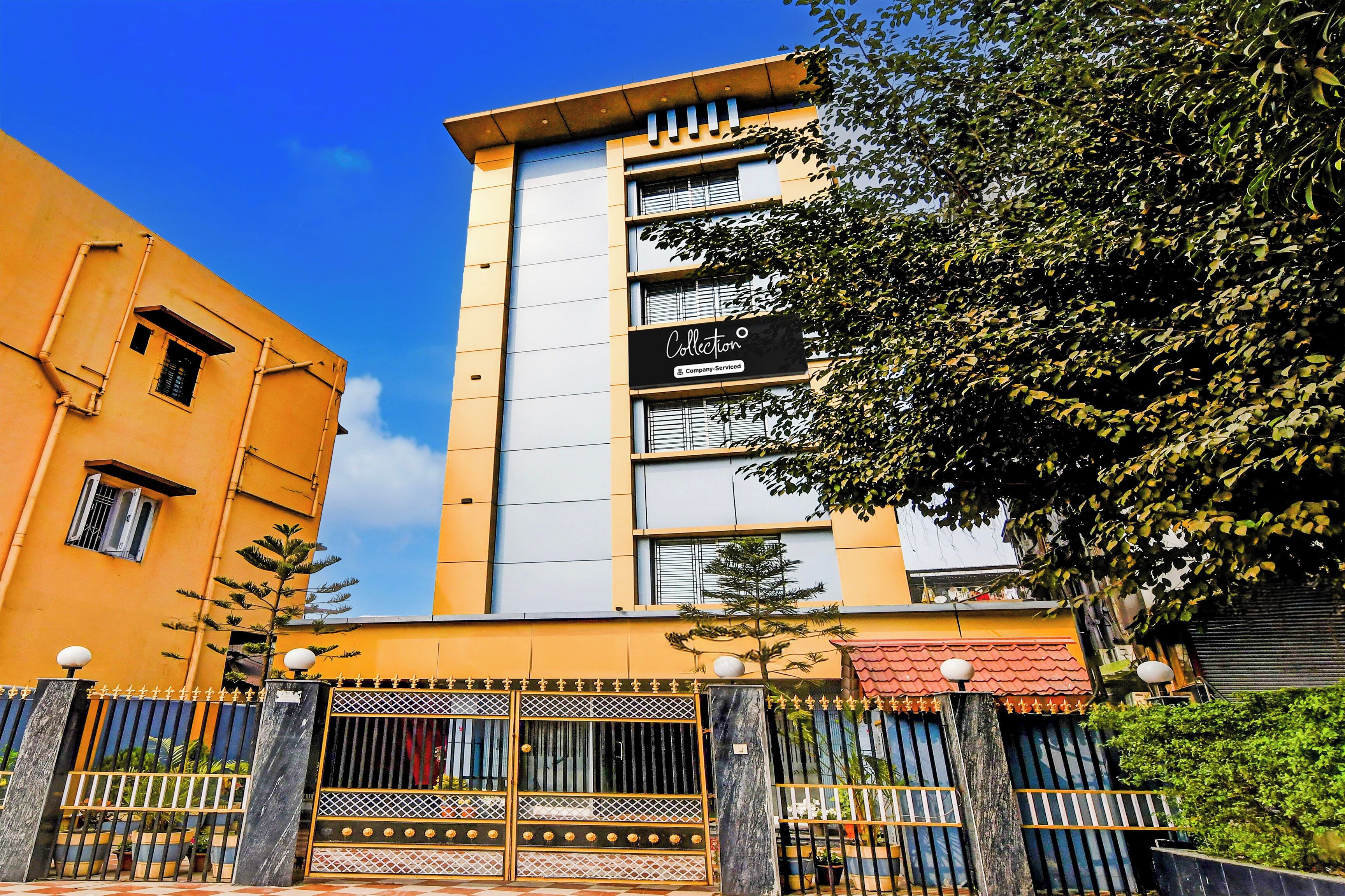 Un edificio de varios pisos con un llamativo letrero 'Collection', una entrada protegida por una reja y un cielo azul despejado.
