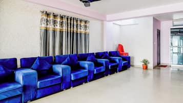 A reception area with a row of blue sofas, a ceiling fan, and a red chair.