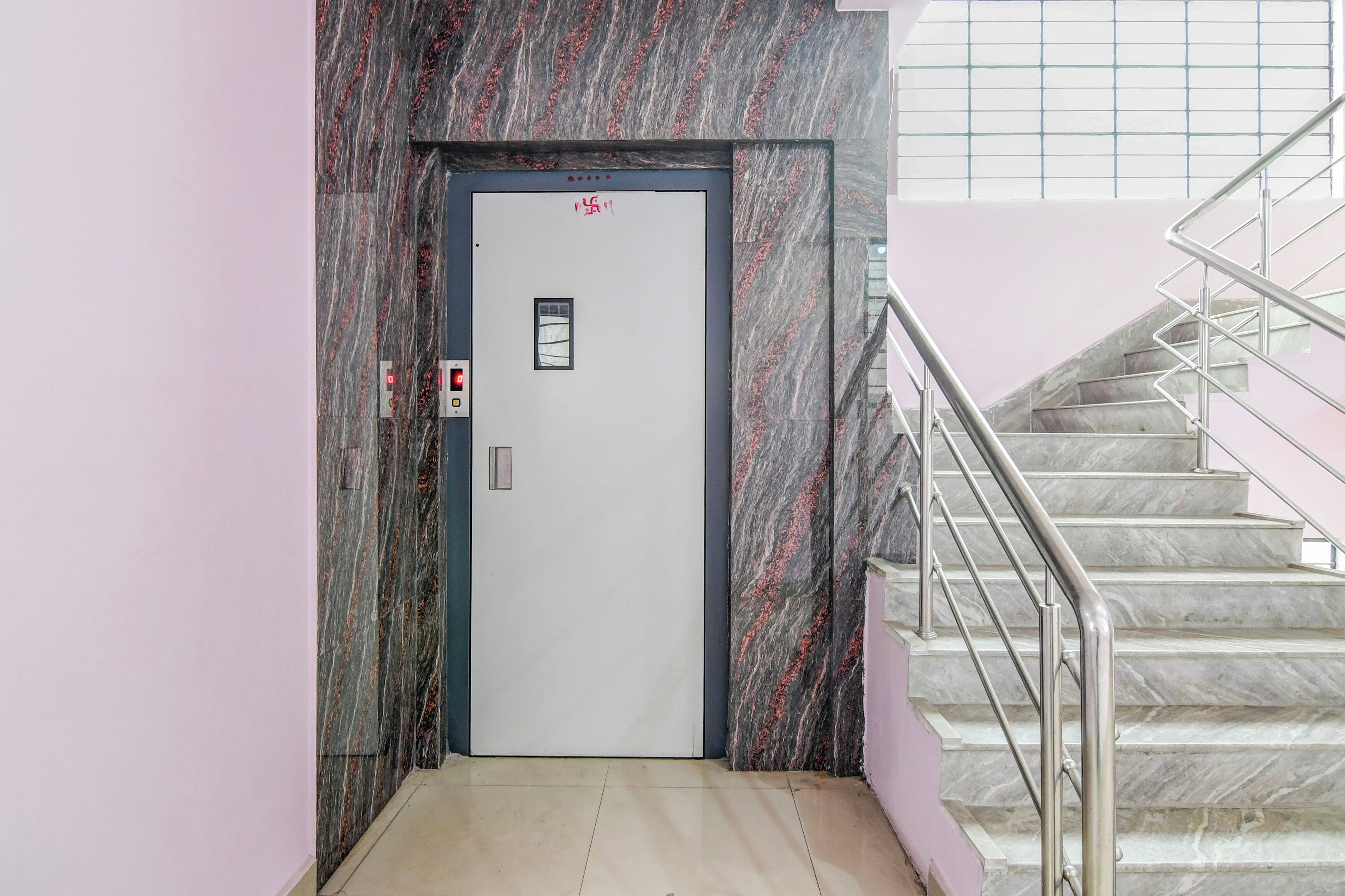 An elevator with a digital display, a door with a red symbol, and a staircase with metal railings.