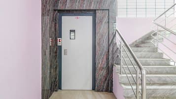 An elevator with a digital display, a door with a red symbol, and a staircase with metal railings.
