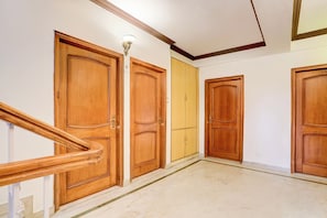 A hallway with wooden doors numbered 106, 107, and 108, a marble floor, and a wooden staircase. - Super Collection O Mall Road (Shimla)