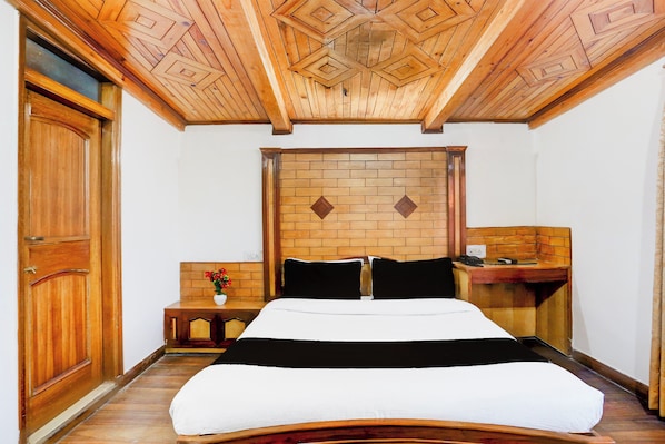 A hotel room with a wooden ceiling, a brick-patterned headboard, a bed with white bedding, a nightstand, and a desk with a telephone. - Super Collection O Mall Road (Shimla)