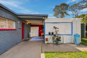Ein Wohnhaus mit Backsteinfassade, einer roten Tür und einer weißen Garagentür. Vor der Garage liegt eine blau-weiß gestreifte Fußmatte, und Kübelpflanzen stehen draußen.