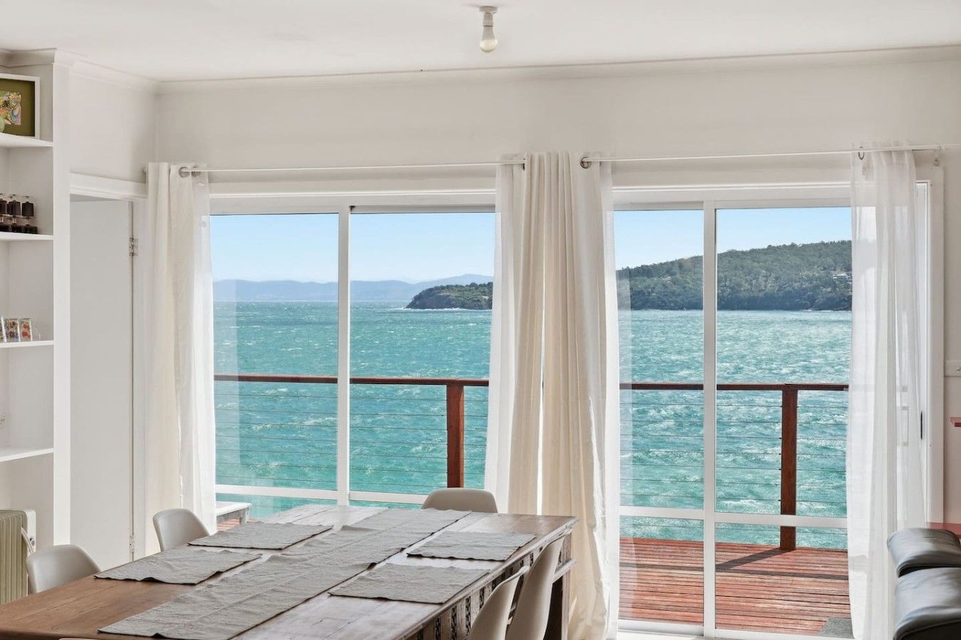 Une pièce dotée d’une grande fenêtre donnant sur la mer, d’une table en bois et offrant une vue sur une île lointaine.