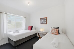 Ein Hotelzimmer mit zwei Betten, einem Nachttisch mit Lampe, einem gerahmten Foto an der Wand und einem Fenster mit Vorhängen.
