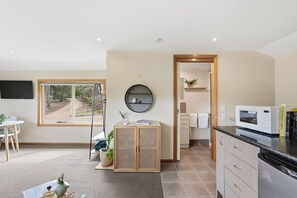 A modern kitchen with a built-in microwave, a dining area with a table and chairs, and a view of the outdoors through a window. - Cosy Bush Studio Near Airport (Acton Park)