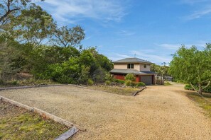 A two-story house with a gravel driveway and a fenced yard. - Cosy Bush Studio Near Airport (Acton Park)