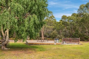 An outdoor seating area with a picnic table and benches, surrounded by trees. - Cosy Bush Studio Near Airport (Acton Park)