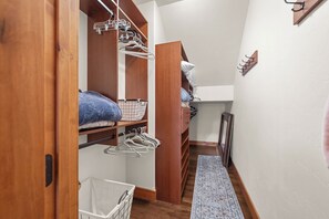 A narrow hallway with wooden flooring, a white wall, and a wooden door leading to a closet with hanging clothes and a basket. - Lakeview Retreat 4BR Home (Somers)