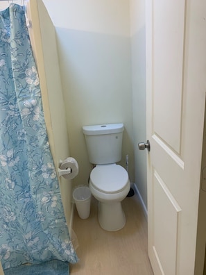 A bathroom with a toilet, a trash bin, and a shower curtain.