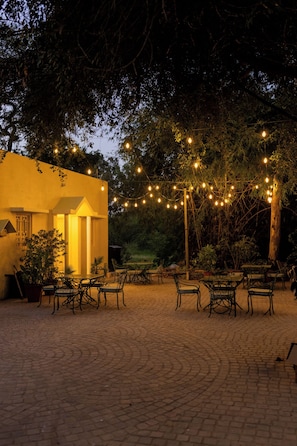 An outdoor seating area with tables and chairs, surrounded by trees and string lights. - The Lake Kingdom (Udaipur)