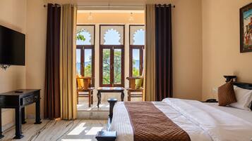 A hotel room with a bed, a desk, a television, and a view of the outdoors through large windows.