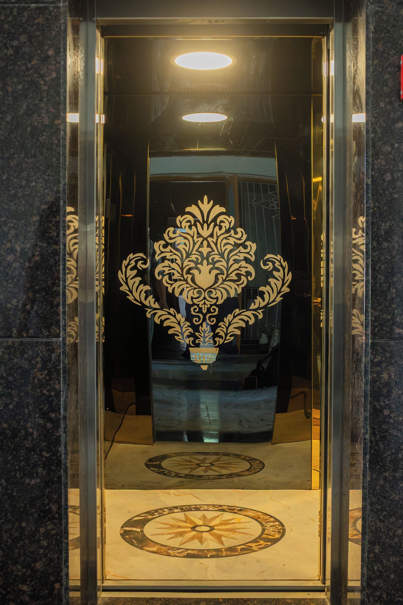 An elevator with a decorative golden emblem on the wall and a marble floor.
