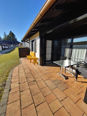 A covered patio area with a table and chairs, a bench, and a view of the street. - Holiday Home 'Erholsamer Urlaub Im Schönen Allgäu' with Private Terrace and Wi-Fi (Lechbruck am See)
