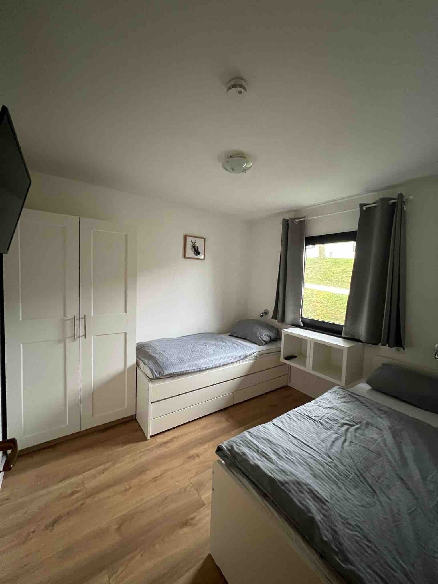 Une chambre à coucher comprenant un lit, une armoire, une table de chevet, une fenêtre avec des rideaux et un luminaire au plafond.