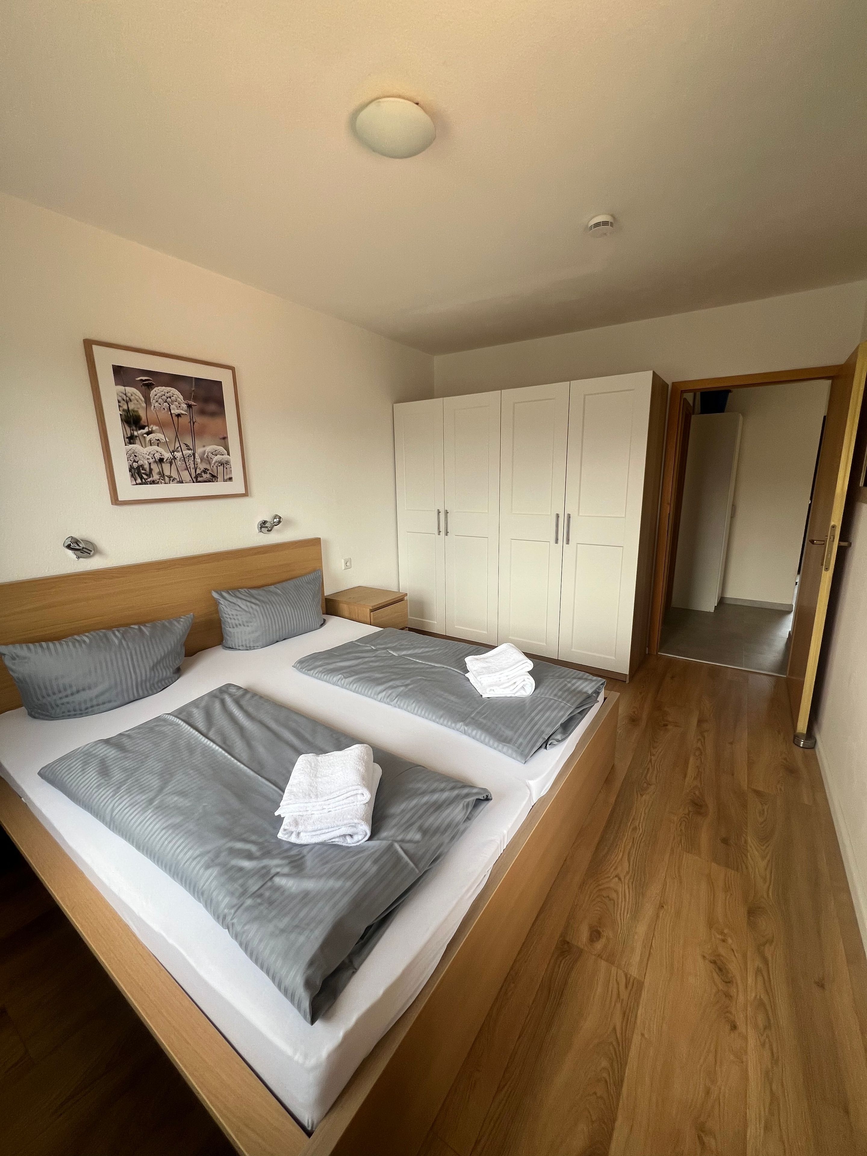 A bedroom with two beds, a wardrobe, and a framed picture on the wall.