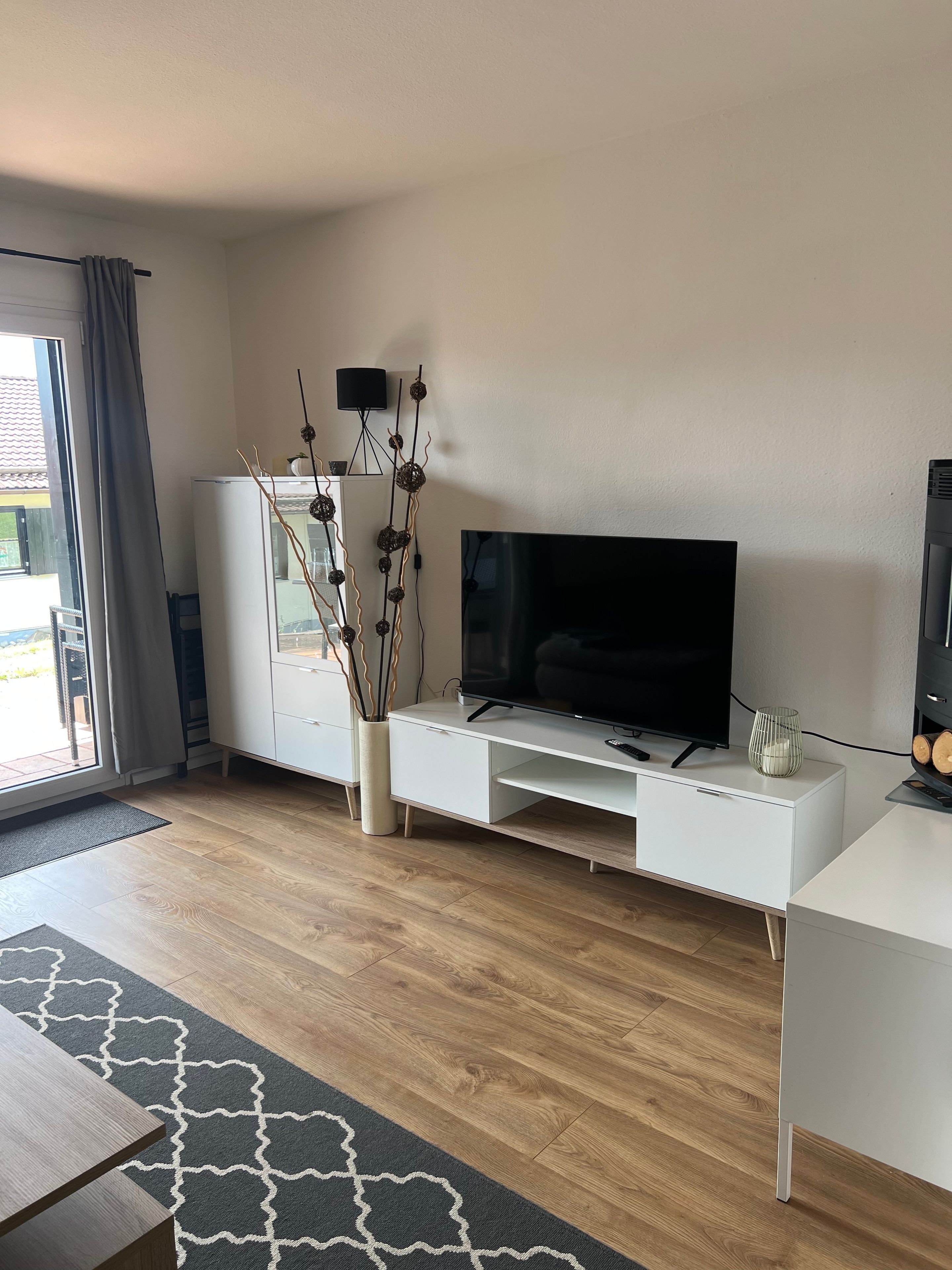 Una sala moderna con un televisor de pantalla plana, un mueble de entretenimiento blanco y una planta decorativa.
